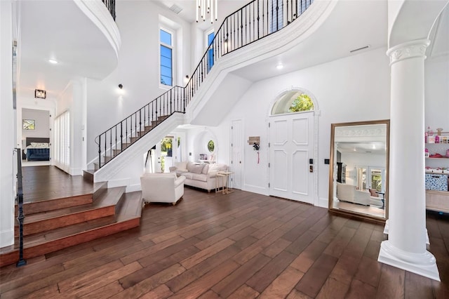 foyer entrance with dark wood finished floors, stairway, a high ceiling, and ornate columns