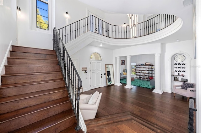 foyer with dark wood finished floors, decorative columns, visible vents, and a towering ceiling