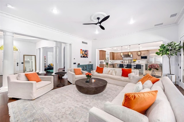 living area with visible vents, a ceiling fan, wood finished floors, crown molding, and ornate columns