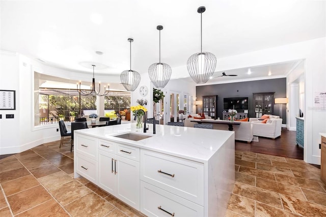 kitchen with an island with sink, a sink, white cabinets, pendant lighting, and a chandelier