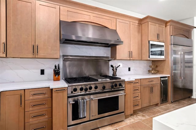 kitchen featuring tasteful backsplash, wine cooler, wall chimney range hood, built in appliances, and light stone countertops