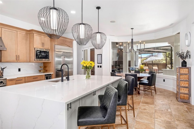 kitchen featuring backsplash, a chandelier, built in appliances, hanging light fixtures, and a sink