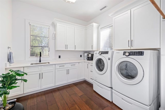 washroom with visible vents, dark wood-type flooring, a sink, cabinet space, and separate washer and dryer