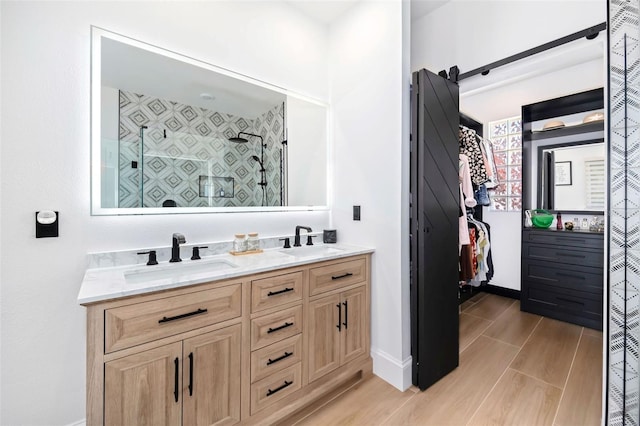 full bath with a sink, wood tiled floor, a stall shower, and double vanity