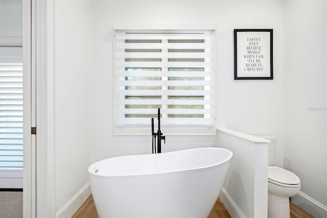 full bath featuring toilet, a freestanding bath, baseboards, and wood finished floors