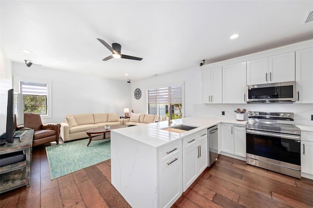 kitchen with a sink, a peninsula, white cabinets, and stainless steel appliances