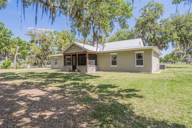 rear view of property featuring stucco siding, cooling unit, metal roof, and a yard