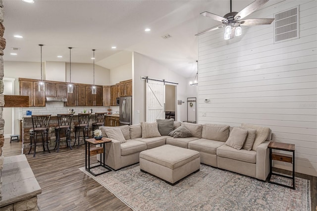 living room featuring high vaulted ceiling, a ceiling fan, wood finished floors, a barn door, and wooden walls