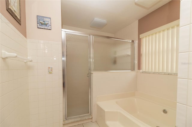 bathroom featuring tile walls, a stall shower, tile patterned floors, and a garden tub