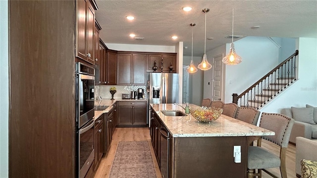 kitchen with a kitchen island with sink, a sink, a kitchen breakfast bar, dark brown cabinets, and light wood-type flooring