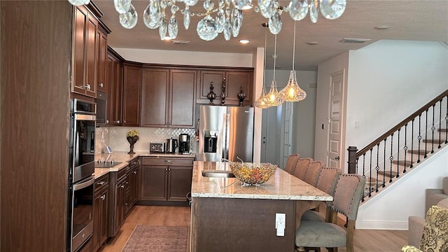 kitchen with an island with sink, light stone counters, stainless steel appliances, light wood-type flooring, and a kitchen bar