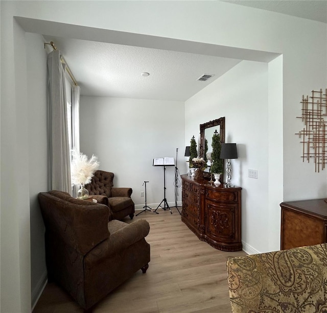 sitting room featuring light wood finished floors, baseboards, visible vents, and a textured ceiling