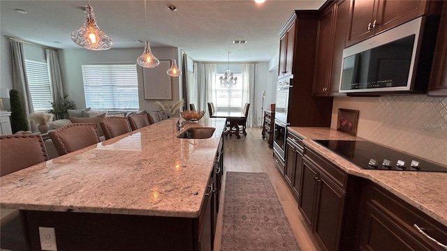 kitchen featuring dark brown cabinetry, stainless steel appliances, a sink, decorative backsplash, and light stone countertops