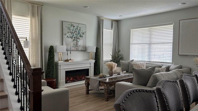 living area featuring a warm lit fireplace, stairs, wood finished floors, and a textured ceiling