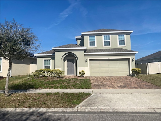 traditional-style home with fence, roof with shingles, stucco siding, decorative driveway, and a garage