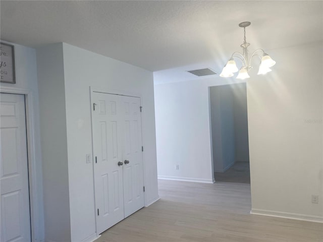 hall with a chandelier, visible vents, baseboards, and light wood-style floors