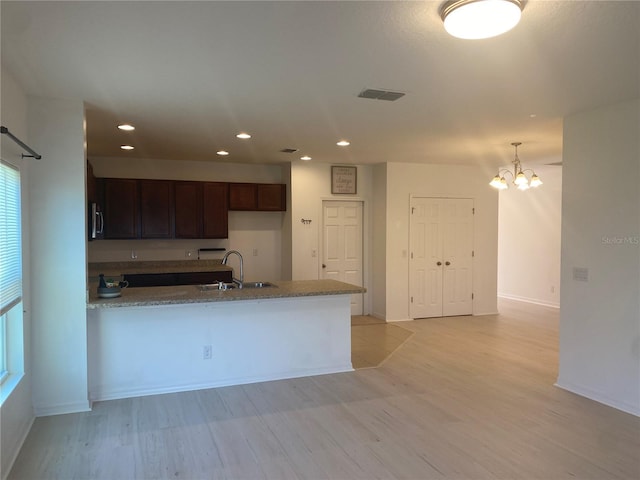 kitchen with a sink, visible vents, light wood-type flooring, and a peninsula