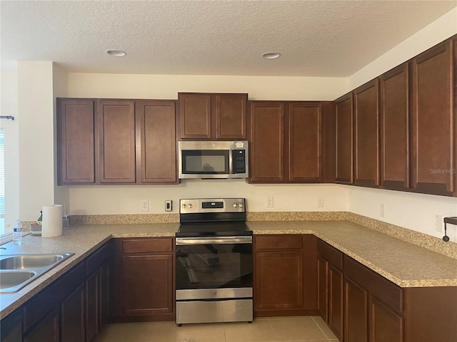 kitchen with dark brown cabinetry, light tile patterned floors, appliances with stainless steel finishes, and a sink