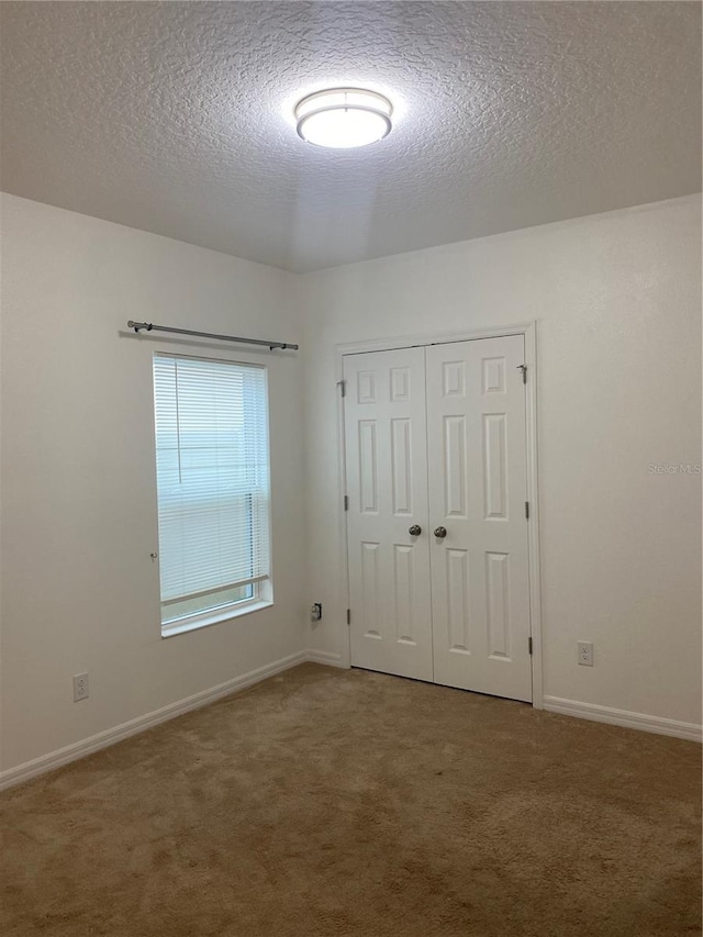 unfurnished bedroom with a closet, a textured ceiling, baseboards, and carpet floors