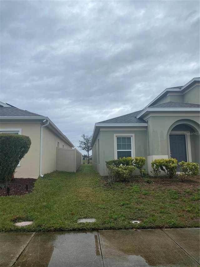 view of property exterior with stucco siding, a lawn, and fence