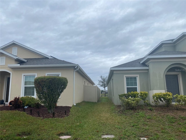 view of side of property featuring a shingled roof, a yard, and stucco siding