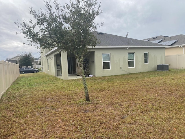 back of house with stucco siding, a lawn, fence, cooling unit, and a shingled roof