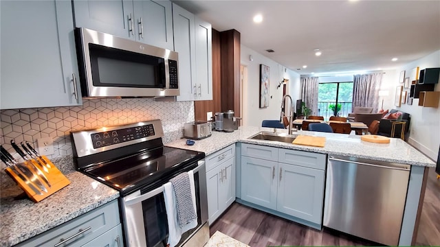 kitchen with decorative backsplash, appliances with stainless steel finishes, open floor plan, a peninsula, and a sink