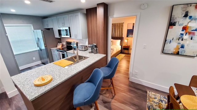 kitchen with stainless steel appliances, dark wood-type flooring, backsplash, light stone countertops, and a kitchen bar