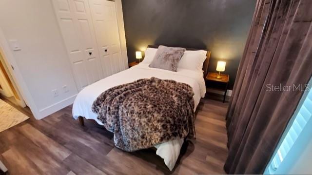 bedroom with a closet, dark wood-style flooring, and baseboards