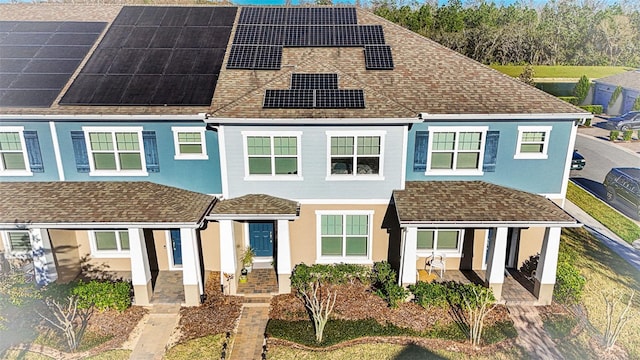 multi unit property with solar panels, a patio, and roof with shingles