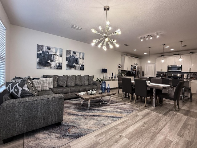 living room with a notable chandelier, a textured ceiling, light wood-type flooring, and visible vents