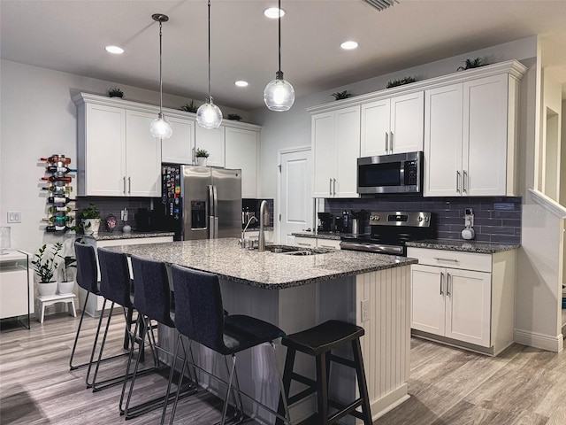 kitchen with light wood finished floors, a breakfast bar, an island with sink, a sink, and appliances with stainless steel finishes