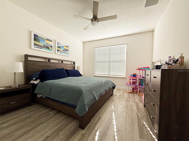 bedroom featuring visible vents, a textured ceiling, ceiling fan, and wood finished floors