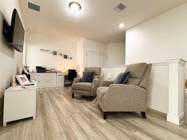 sitting room featuring visible vents, baseboards, a textured ceiling, and light wood finished floors