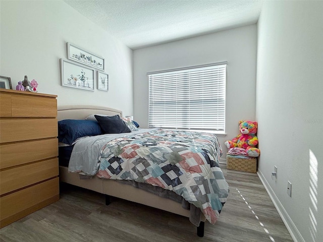 bedroom with wood finished floors, baseboards, and a textured ceiling