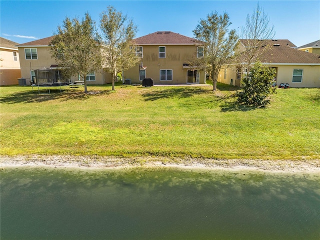 back of property with a trampoline, a lawn, and stucco siding