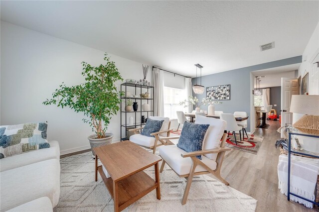 living room featuring baseboards, visible vents, light wood finished floors, and a textured ceiling