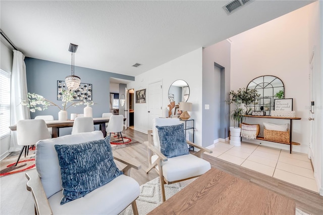 living area featuring visible vents, baseboards, a textured ceiling, and light wood finished floors