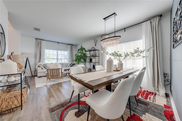 dining space featuring visible vents, baseboards, a chandelier, wood finished floors, and a textured ceiling