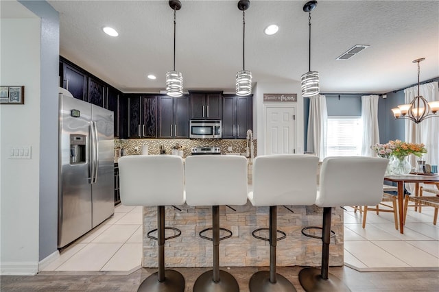 kitchen featuring visible vents, backsplash, decorative light fixtures, stainless steel appliances, and a textured ceiling