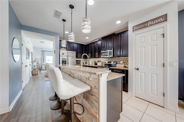 kitchen featuring light stone countertops, visible vents, a breakfast bar, stainless steel appliances, and backsplash