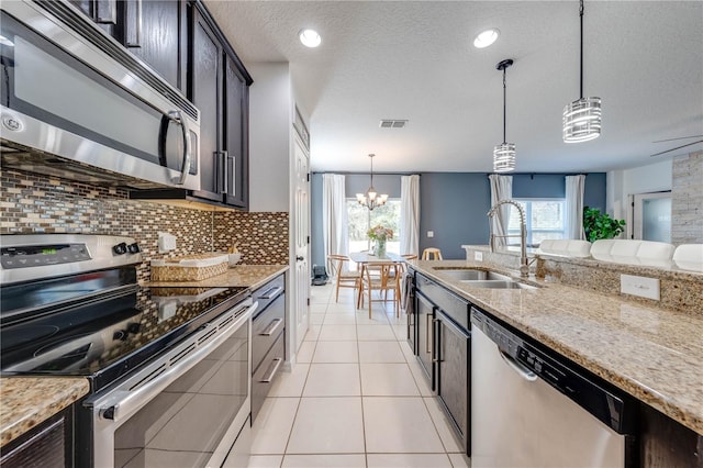 kitchen with light tile patterned floors, light stone countertops, a sink, stainless steel appliances, and backsplash