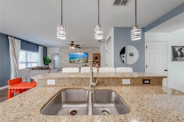 kitchen with light stone counters, decorative light fixtures, a textured ceiling, and a sink