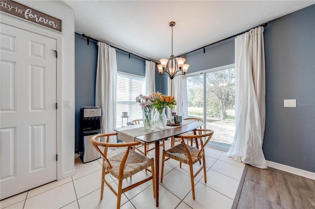 dining room with light wood-type flooring, baseboards, a notable chandelier, and a textured ceiling