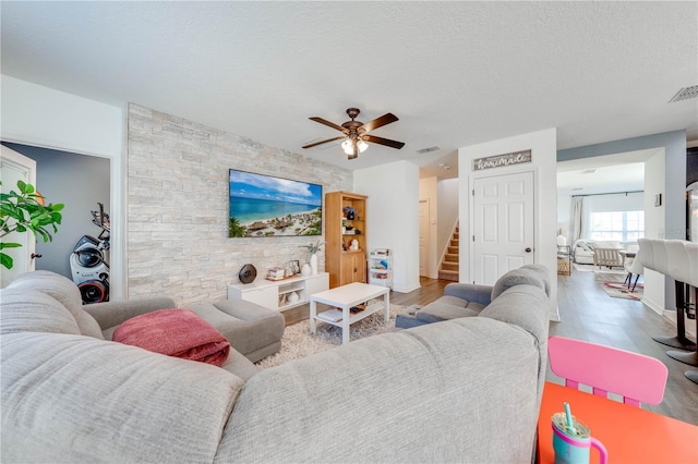 living area with stairway, a ceiling fan, wood finished floors, visible vents, and a textured ceiling