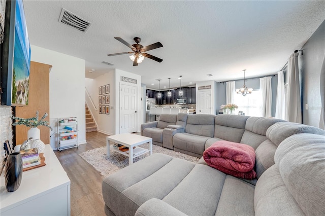 living room featuring visible vents, ceiling fan with notable chandelier, a textured ceiling, wood finished floors, and stairs