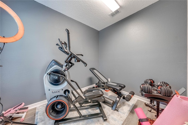 exercise area with visible vents, baseboards, a textured ceiling, and wood finished floors