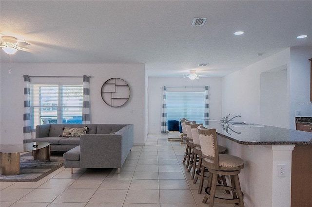 living room featuring a textured ceiling, light tile patterned floors, visible vents, and ceiling fan