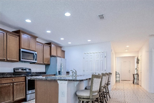 kitchen featuring a breakfast bar, a center island with sink, a sink, dark stone countertops, and stainless steel appliances