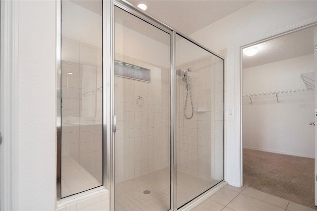 bathroom with tile patterned flooring, a spacious closet, and a stall shower